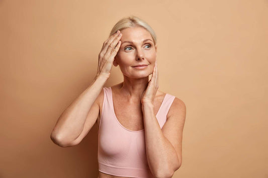 A portrait of a mature elderly European woman who gently touches her face, showcasing perfect skin, looking thoughtfully away as she enjoys her soft complexion, cares about her appearance, and feels satisfied after an anti-aging procedure.